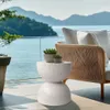 A white speckled hourglass-shaped side table with two potted succulents sits on a patio overlooking a body of water and mountains. Podgląd zdjęcia produktu