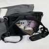 Schwarze Nylon-Umhängetasche mit geöffnetem Hauptfach, darin sichtbar ein Smartphone, Kosmetik und eine gestreifte Tasche Produktbild-Vorschau