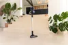 A cordless stick vacuum cleaner stands on a light-colored staircase in a modern home setting. Náhľad obrázku produktu