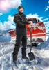 A man in work clothes stands in the snow with a snow plow behind him. Anteprima dell’immagine prodotto