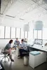 Three people are gathered around a desk in a modern office, discussing documents. Podgląd zdjęcia produktu