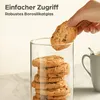 A hand is taking a cookie from a stack of cookies inside a glass jar, with a mug in the background. Produktbild-Vorschau