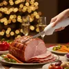 Weißes elektrisches Tranchiermesser schneidet einen glasierten Schinken an einer festlichen Tafel mit Sektgläsern und verschwommenen Lichtern Anteprima dell’immagine prodotto