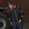 A man wearing work clothes and gloves stands next to a tractor. Produktbild-Vorschau