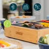 A close-up of a table grill with food being cooked on it, set on a table with other food items in bowls. Produktbild-Vorschau