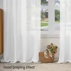 A white sheer curtain is shown draped in front of a window, with a wicker basket containing flowers placed on the floor in the foreground. Produktbild-Vorschau