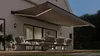 An outdoor patio area with a table and chairs set up under a retractable awning with integrated LED lighting. Produktbild-Vorschau