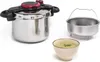 A stainless steel pressure cooker with a red and black lid, a steaming basket, and a bowl of soup are displayed against a white background. Náhľad obrázku produktu