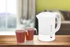 A white electric kettle and two cups of tea are placed on a wooden table in front of a blurred background of a living room. Voir les images du produit
