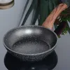 A close-up shot of a frying pan with a wooden handle, set against a blurred background of greenery and a light-colored object. Podgląd zdjęcia produktu