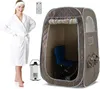 A woman in a white robe stands next to a portable steam sauna tent, a steam generator, and a remote control. Náhľad obrázku produktu