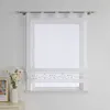 A white sheer Roman blind with a floral embroidered border hangs on a window. Produktbild-Vorschau