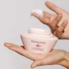A hand is shown holding a jar of hair mask, with some product on a finger. Náhled obrázku produktu