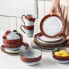 A set of ceramic dishes, including plates, bowls, and mugs, arranged on a white surface. A person's hands are visible arranging a stack of plates. Náhled obrázku produktu