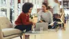 Two women are sitting on chairs in a modern office space, looking at a laptop and papers on a glass table. Produktbild-Vorschau