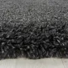 A close-up, low-angle view of a dark gray shaggy rug with a light gray wooden floor visible beneath it. Produktbild-Vorschau