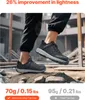 A person wearing black work pants and black safety sneakers is walking on a pile of dirt and rocks. The sneakers have a gray sole and a black upper with a geometric pattern. The image highlights the lightness of the shoes. Produktbild-Vorschau