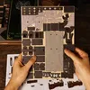 Hands holding a 3D puzzle kit for a book nook, with instructions visible below. Voir les images du produit