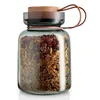 A glass storage jar filled with granola, with a wooden lid and a leather strap. Produktbild-Vorschau