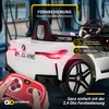 A white electric BMW i4 toy car with a red remote control in the foreground. Produktbild-Vorschau
