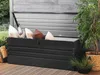 An open black garden storage box filled with cushions, placed on a wooden deck next to a potted plant. Náhled obrázku produktu
