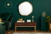 A stylish living room with a dark green wall, featuring a gold-rimmed abstract mirror, a dark wood console table with decorative items, and a green velvet sofa. Podgląd zdjęcia produktu