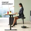 A woman in a suit sits at a standing desk and works on a laptop, with a wobble stool. Náhled obrázku produktu