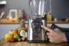 A hand is shown adjusting the settings on a Tefal blender, surrounded by fresh fruits. Podgląd zdjęcia produktu