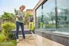 A woman is using a pressure washer to clean a patio in front of a modern house. Produktbild-Vorschau