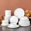 A collection of white ceramic dinnerware with black trim, arranged on a table. Produktbild-Vorschau