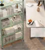 A green metal shelving unit filled with books and decorative items, next to a white desk with a laptop and fruit bowl. Produktbild-Vorschau