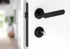 A close-up view of a black door handle and lock set on a white door. Produktbild-Vorschau