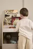A young child is looking at a bookshelf filled with books and toys. Produktbild-Vorschau