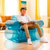 A young boy is playing a video game while sitting on a transparent blue inflatable chair in a living room. Produktbild-Vorschau