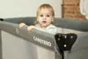 A baby is standing in a gray playpen. Anteprima dell’immagine prodotto