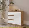 A modern sideboard with white gloss drawers and a wood-effect frame, placed in a room setting with a plant and a lamp. Voir les images du produit