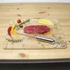 A raw steak, herbs, chili peppers, and a meat injector are arranged on a wooden cutting board. Produktbild-Vorschau