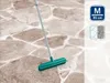 A floor broom with a green head and a gray handle is shown on a stone-like floor. Produktbild-Vorschau