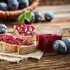 A rustic scene with plum jam on bread, a jar of jam, and fresh plums on a wooden table. Náhled obrázku produktu