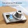 A silver digital camera is placed on a sandy beach with a tropical scene displayed on its screen. Produktbild-Vorschau