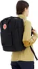 A person wearing a tan jacket and navy pants is wearing a black backpack. Anteprima dell’immagine prodotto