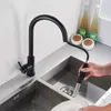 A person is using a black kitchen faucet with a pull-down sprayer to wash dishes in a double stainless steel sink. Produktbild-Vorschau