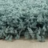 A close-up view of a shaggy teal rug with a light wooden floor visible underneath. Produktbild-Vorschau