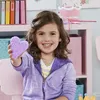 A young girl is smiling and holding a purple heart-shaped object made of small beads. Produktbild-Vorschau