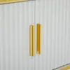A close-up view of two gold handles on a white fluted cabinet. Podgląd zdjęcia produktu