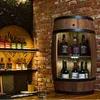 A wooden barrel-shaped bar cabinet filled with bottles of alcohol, set against a brick wall. Náhled obrázku produktu