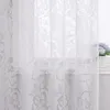 A close-up view of a white sheer curtain with a floral pattern, partially covering a window. Produktbild-Vorschau