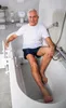 An elderly man sits in a bathtub with a bath seat. Produktbild-Vorschau