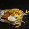 A plate of fish and chips with a side of sauce and lemon wedges, served on newspaper. Produktbild-Vorschau