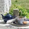 A tea set laid out on a table outdoors, with greenery in the background. Produktbild-Vorschau